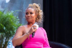 Gizelle Bryant in a pink dress with a microphone in her hand looking to the side