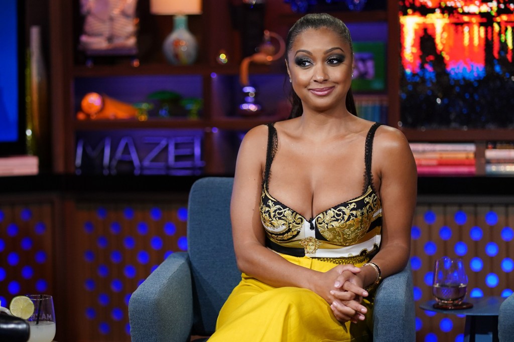 Eboni K. Williams sitting with her legs crossed on Watch What Happens Live, wearing yellow pants and a black bustier.
