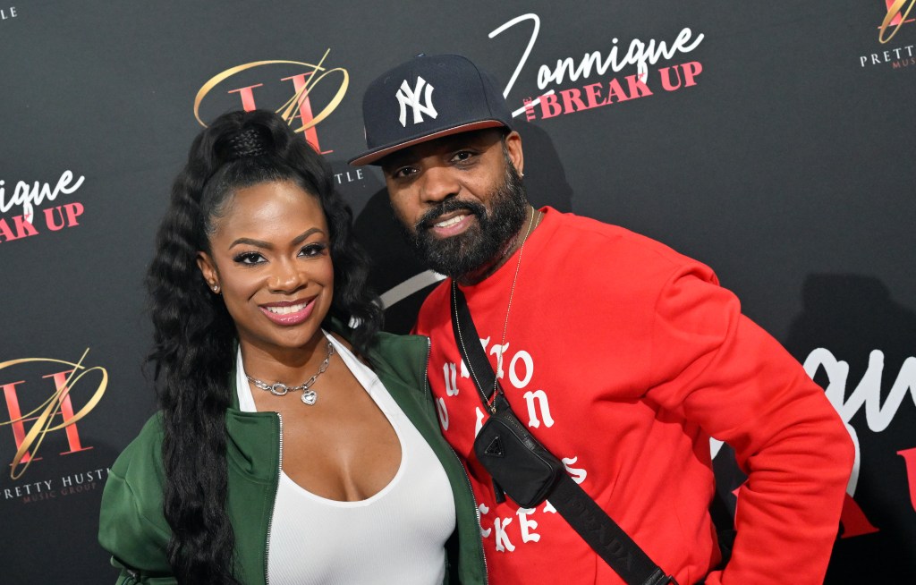 Kandi Burruss and Todd Tucker posing together; Kandi is wearing a green jacket with a white T-shirt. Todd is wearing a red sweater and a New York Yankees hat.