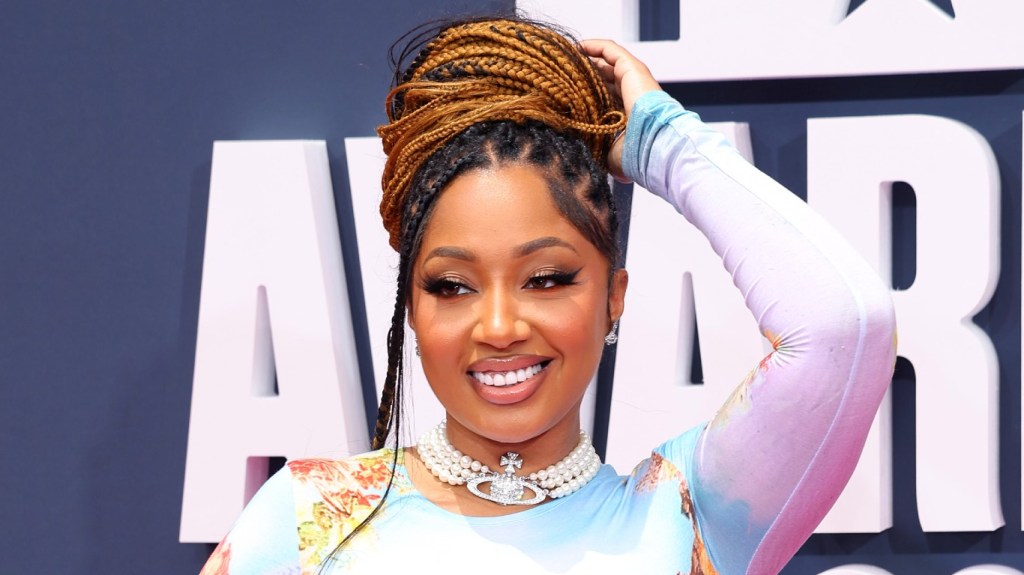 Brittish Williams smiling and wearing a colorful dress, posing with her hand on her hand