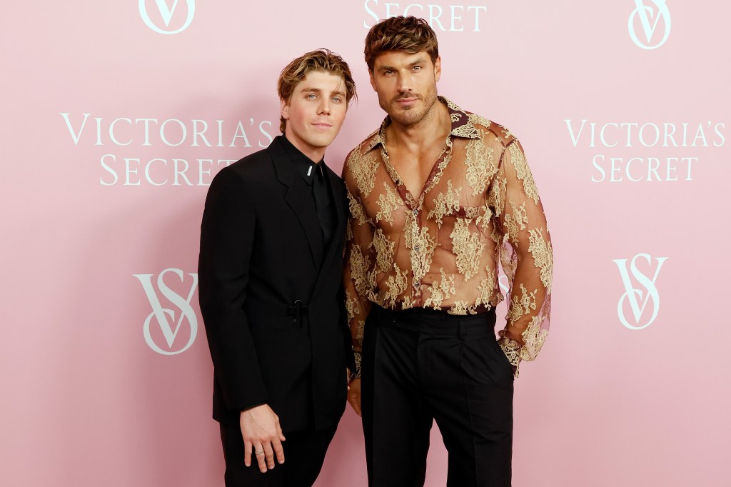 Lukas Gage in a black suit standing with Chris Appleton who's wearing a gold sheer top.