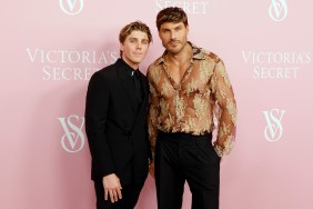 Lukas Gage in a black suit standing with Chris Appleton who's wearing a gold sheer top.