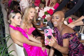 Guery Abraira in a purple dress holding up her phone and showing it to Lisa Hochstein and Dr. Nicole Martin, who are both wearing pink dresses. Lisa has a surprised expression on her face.