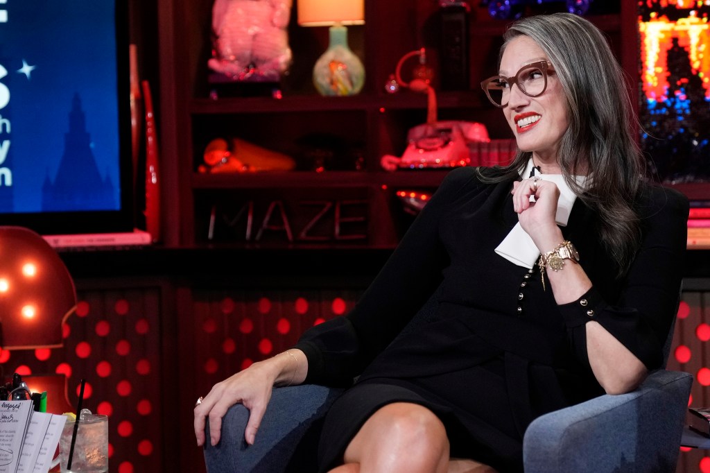 Jenna Lyons on watch What Happens Live, smirking while wearing a black dress with a white collar