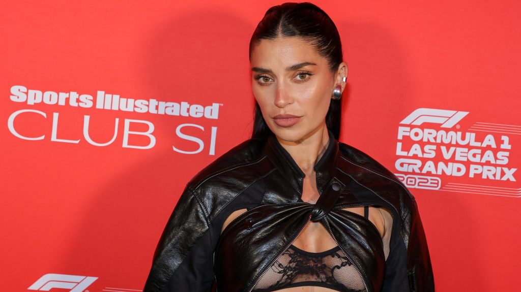 Nicole Williams English in front of a red back drop in a black leather bra and jacket