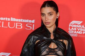 Nicole Williams English in front of a red back drop in a black leather bra and jacket