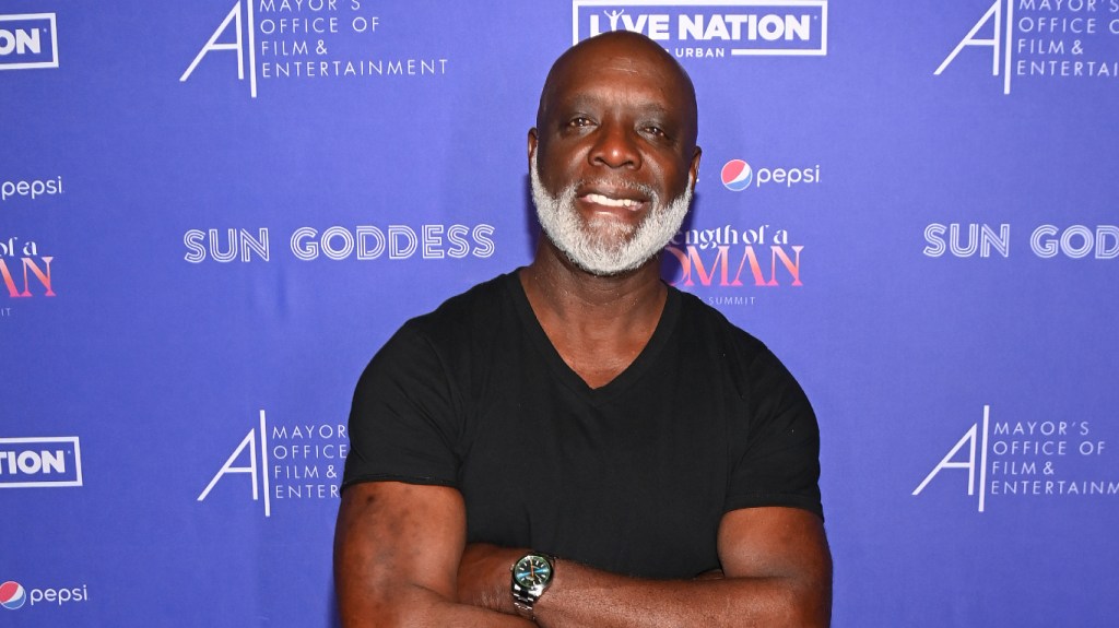 Peter Thomas in a black shirt, smiling, and posing with his arms crossed