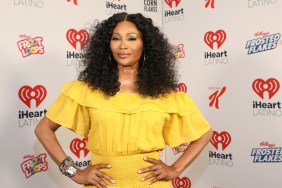 Cynthia Bailey smiling and standing with her hands on her hips, wearing a yellow dress.