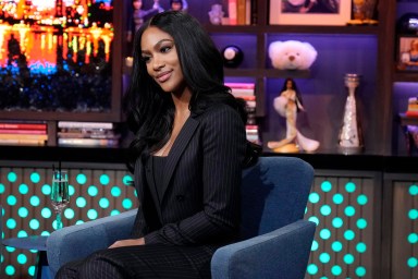 Jordan Emanuel on Watch What Happens Live, wearing a black dress, smiling, and tilting her head to the side.
