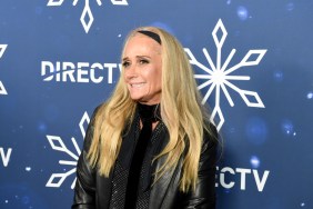 Kim Richards wearing a black jacket and headband, smiling, and standing in front of a blue backdrop with snowflakes