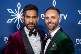 Amrit Kapai in a red blazer standing with husband Nicholas Kouchoukos who's wearing a green blazer