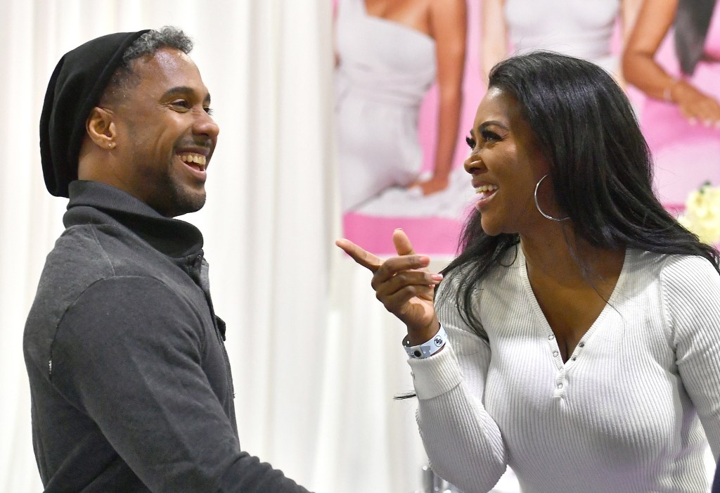 Marc daly on the left in a grey shirt smiling; Kenya Moore is on the right side smiling and pointing at him while wearing a white sweater