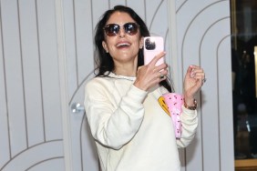 Bethenny Frankel in a white sweater and sunglasses, holding up her phone and smiling