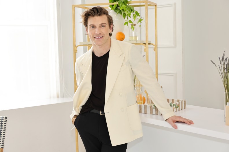 Jeremiah Brent in a white blazer and black shirt, smiling and standing in front of a gold shelf
