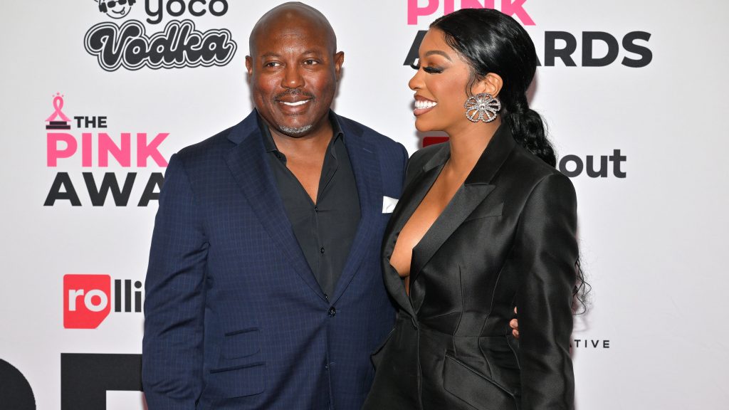 Simon and Porsha Williams Guobadia posing together at a red carpet event; Simon is wearing a blue suit while Porsha is wearing a black suit and looking at Simon from the side