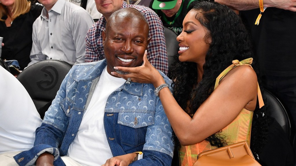 Simon Guobadia and Porsha Williams sitting courtside at a basketball game, they're both smiling and she has her hand on his face