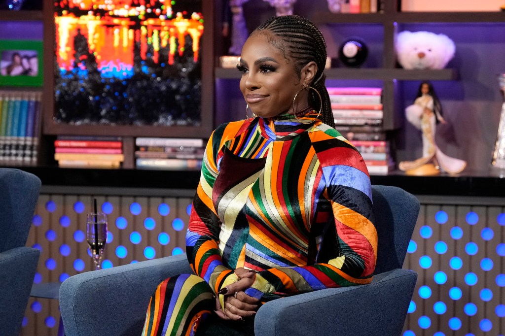 Candiace Dillard Bassett on Watch What Happens Live, smirking and wearing a multicolored jumpsuit