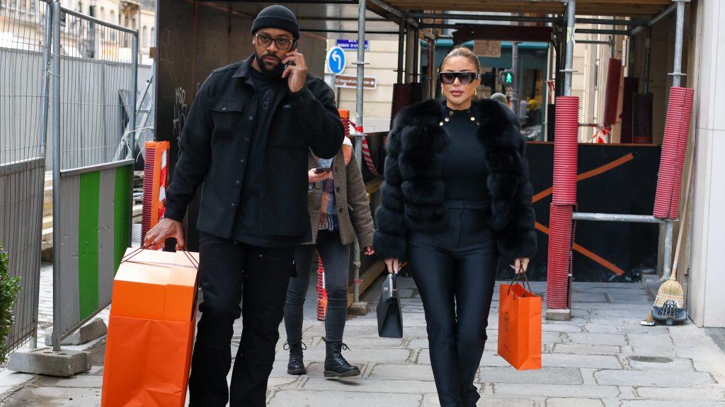 Marcus Jordan and Larsa Pippen dressed in all black and walking outside while carrying orange shopping bags