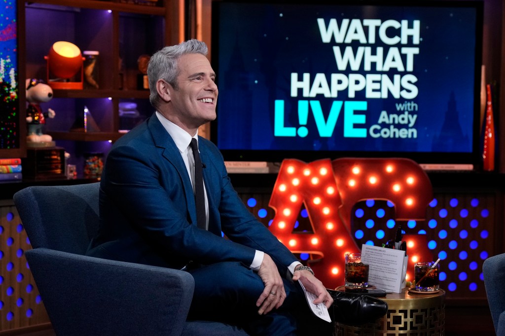 Andy Cohen in a navy blue suit smiling on the set of Watch What Happens Live