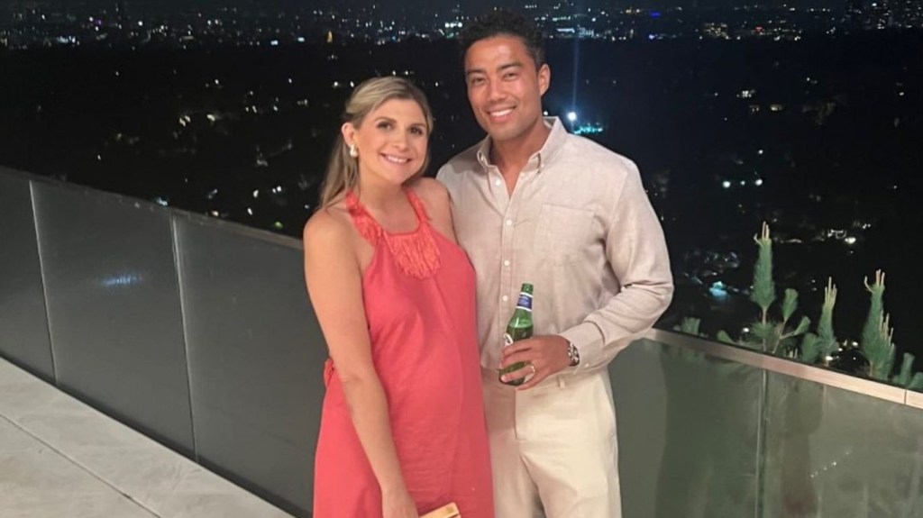 Janet and Jason Caperna standing arm in arm; Janet is wearing a pink dress and Jason is wearing khakis and holding a beer.