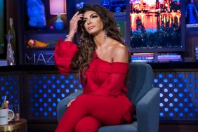 Teresa Giudice in a red jump suit, posing with her legs crossed while fixing her hair on an episode of Watch What Happens Live