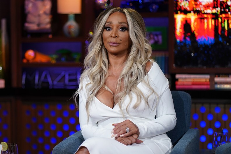 Karen Huger sitting on Watch What Happens LIve, wearing a white dress and making a blank facial expression