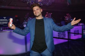 Tom Schwartz in a blue suit holding his arms up in the air while holding a canned beverage