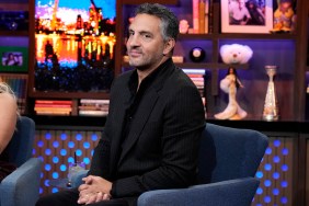 Mauricio Umansky looking out of the side of his eyes and slightly smiling on Watch What Happens Live; he's wearing a black pinstriped suit