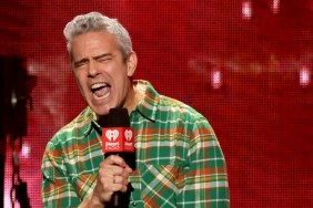 Andy Cohen in a green flannel shirt on stage screaming into a microphone with his eyes shut