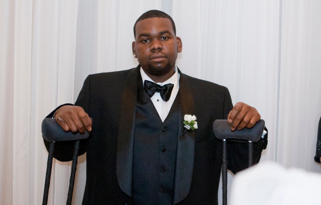 Bryson Bryant in a black tuxedo, smiling, and propping himself up on a set of crutches