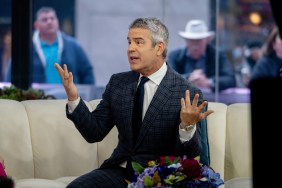 Andy Cohen in a navy blue suit throwing his hands up during an appearance on The Today Show