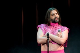 Jonathan Van Ness frowning and standing with their arms crossed in a pink outfit