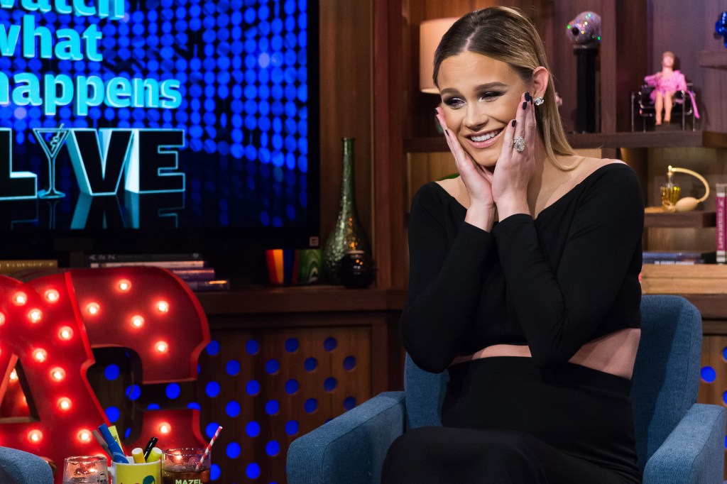 Meghan King in a black dress on Watch What Happens Live smirking and holding her face in her hands