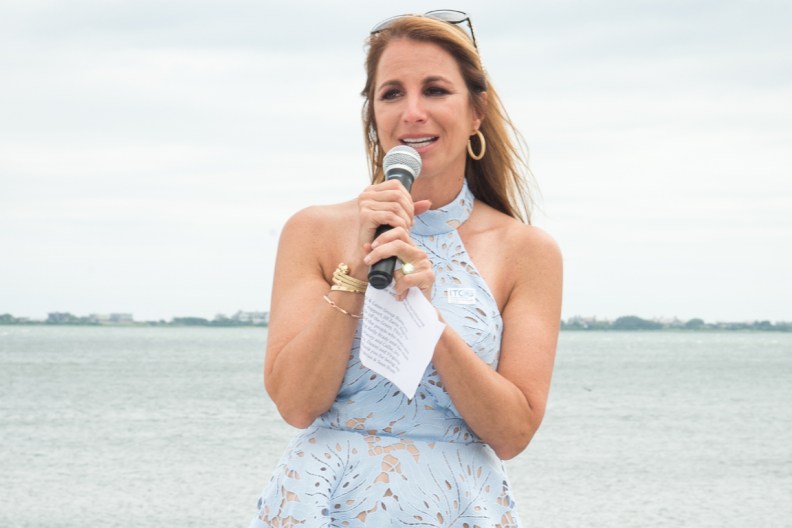 Jill Zarin in a blue dress standing in front of water and speaking into a microphone