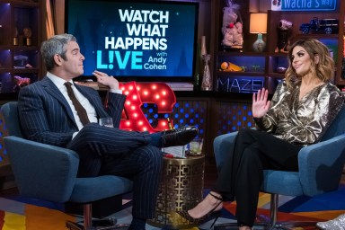 Andy Cohen holding his hands up and sitting across from Lisa Rinna on Watch What Happens Live