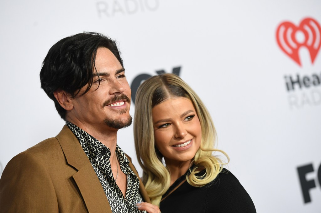 Tom Sandoval in a brown jacket posing with Ariana Madix, who is wearing black at an iHeartRadio event