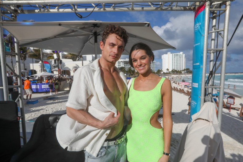 James Kennedy in an unbuttoned white shirt posing on the beach with Ally Lewber, who is wearing a green dress
