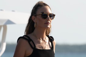 Elizabeth Chambers in a black tank top and black sunglasses walking on the beach