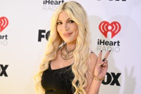Tori Spelling posing in a black dress and holding up the peace sign