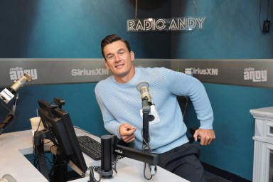 Tyler Cameron sitting in a blue sweater in a Sirius XM studio, leaning into the desk