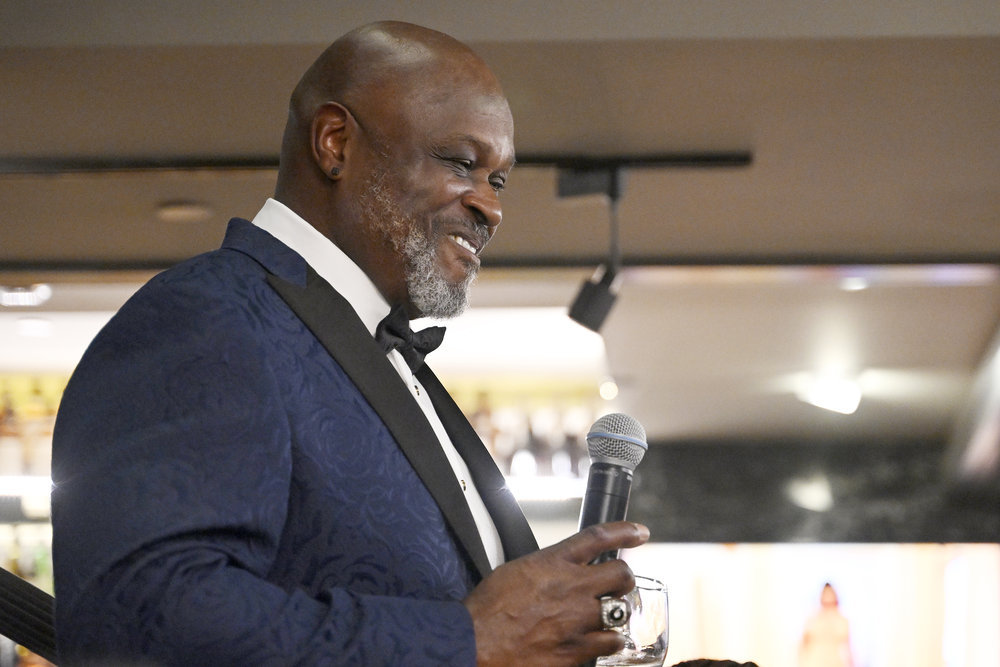 Gordon Thornton smiling and holding a microphone while wearing a navy blue suit