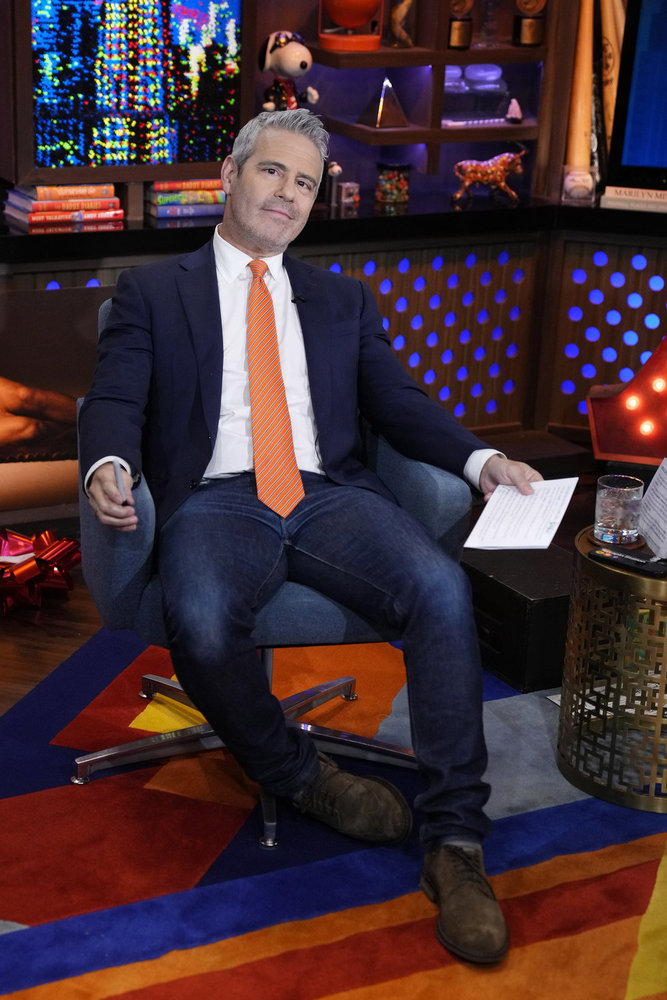 Andy Cohen in jeans and a suit coat, leaning in his chair on Watch What Happens Live