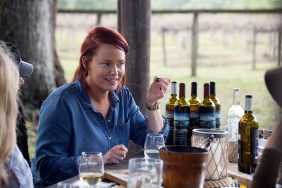 Kathryn Dennis in a blue shirt sitting around a bunch of wine bottles on Southern Charm Season 6