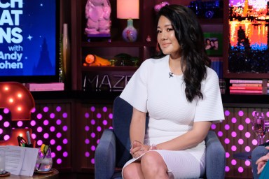 Crystal Kung Minkoff sitting in a white dress with her legs crossed on Watch What Happens Live