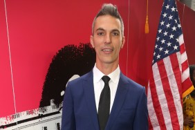 Ari Shapiro in a navy blue suit standing in front of a USA flag