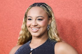 Nia Sioux posing in front of an orange backdrop, she's smiling and wearing a black dress