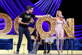 Danielle Cabral in a pink jumpsuit on stage at BravoCon with Jerry O'Connell who is holding her hand while she speaks into a microphone