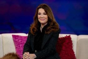 Lisa Vanderpump in a black suit sitting on a white couch with a pink pillow