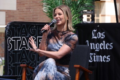 Ariana Madix sitting on an outdoor stage talking into a microphone