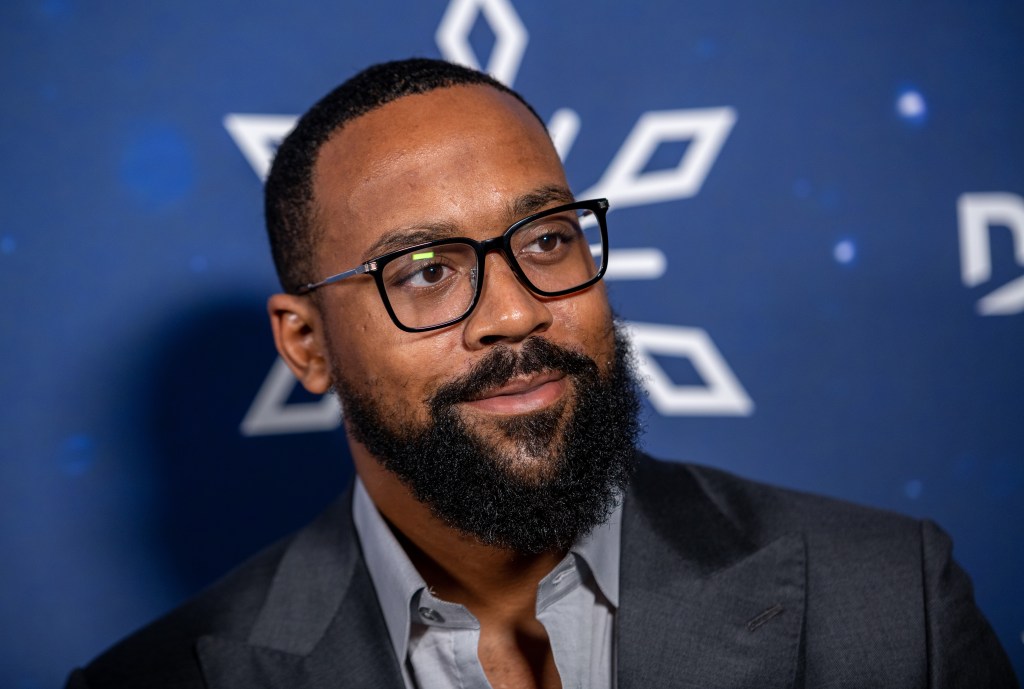Marcus Jordan in a grey suit posing in front of a blue backdrop
